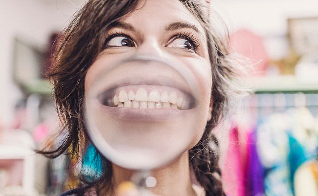 Happy woman goofing around with a magnifying glass in front of her mouth to show her big toothy grin.